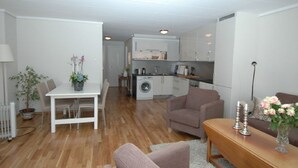 A compact living space with a dining area, a sofa, a small table, a washing machine, and a kitchenette. - Solferie Holiday Apt. Kronprinsensgate (Kristiansand)