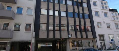 Un immeuble à plusieurs étages doté d’une façade moderne, avec de grandes fenêtres et une entrée au niveau du sol, dont la devanture est bien visible.