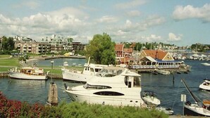 A marina with several boats docked, a building with a red roof, and a grassy area in the foreground. - Solferie Holiday Apt. Kronprinsensgate (Kristiansand)