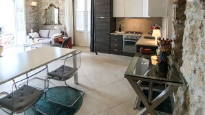 A modern kitchen with a stone wall, a dining area with a glass table, and a living room with a sofa and a lamp. - Calarossa beachfront apartment (Syracuse)