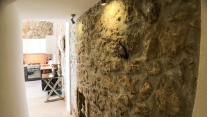 A hallway with a stone wall, a kitchen in the background, and a dining area with a table and chairs. - Calarossa beachfront apartment (Syracuse)