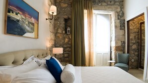 A hotel room with a large bed, a stone wall, a painting, a lamp, and a chair. - Calarossa beachfront apartment (Syracuse)