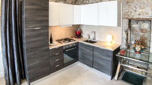 A modern kitchen with dark cabinetry, a gas stove, and a built-in oven. - Calarossa beachfront apartment (Syracuse)