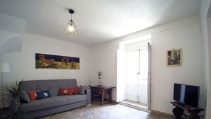A living room with a grey sofa, a potted plant, a painting, a television, and a tiled floor. - Casa Levante (Syracuse)