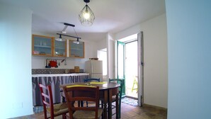 A compact kitchen with a dining area, a refrigerator, and a hanging light fixture. - Casa Levante (Syracuse)