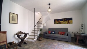 A living room with a staircase, a grey sofa with decorative pillows, a painting on the wall, and a potted plant. - Casa Levante (Syracuse)