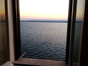 Une vue à travers une fenêtre sur une étendue d’eau, avec une côte et des montagnes qui se dessinent à l’horizon.