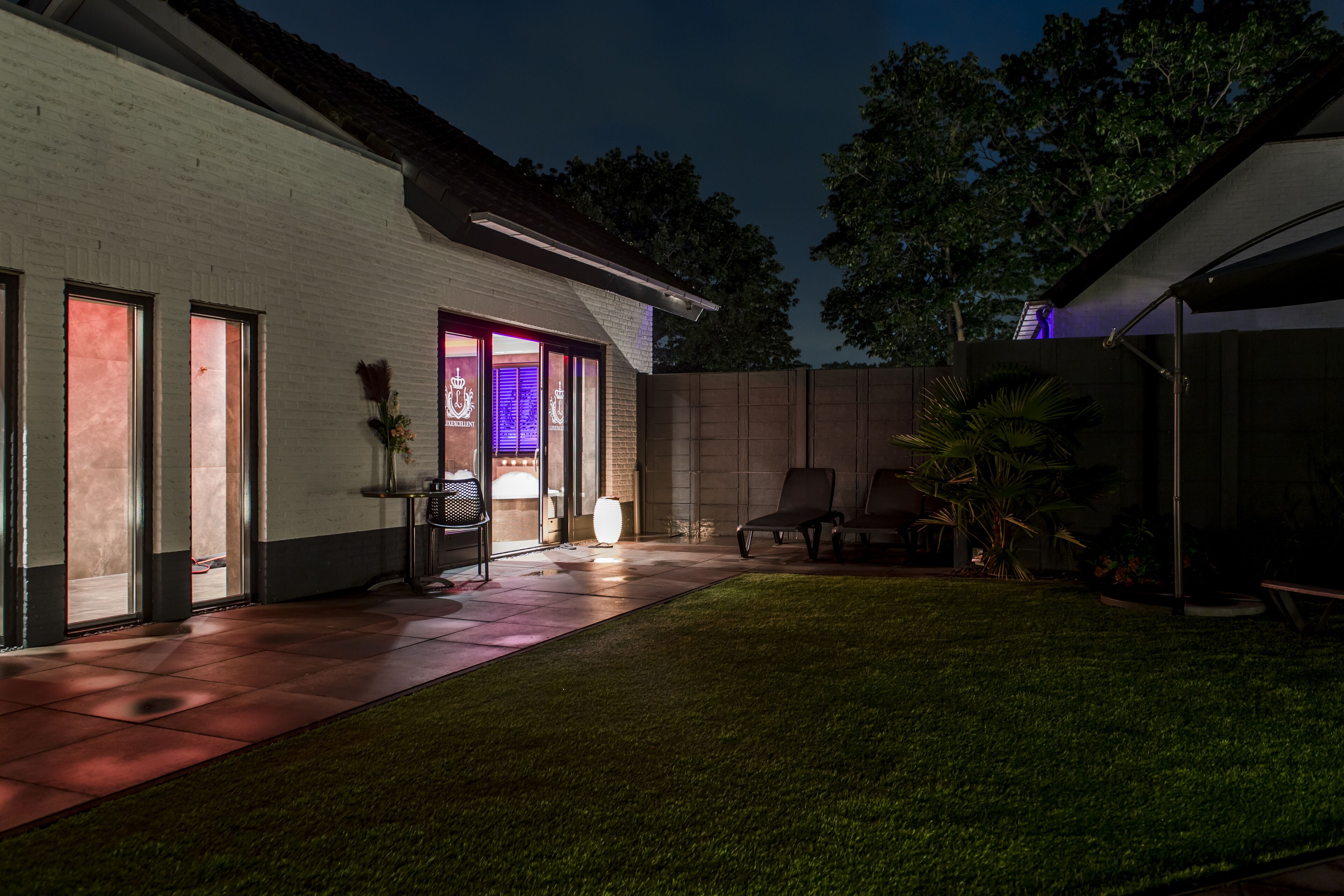A well-lit patio area with a white building, a grassy lawn, and a covered seating area.