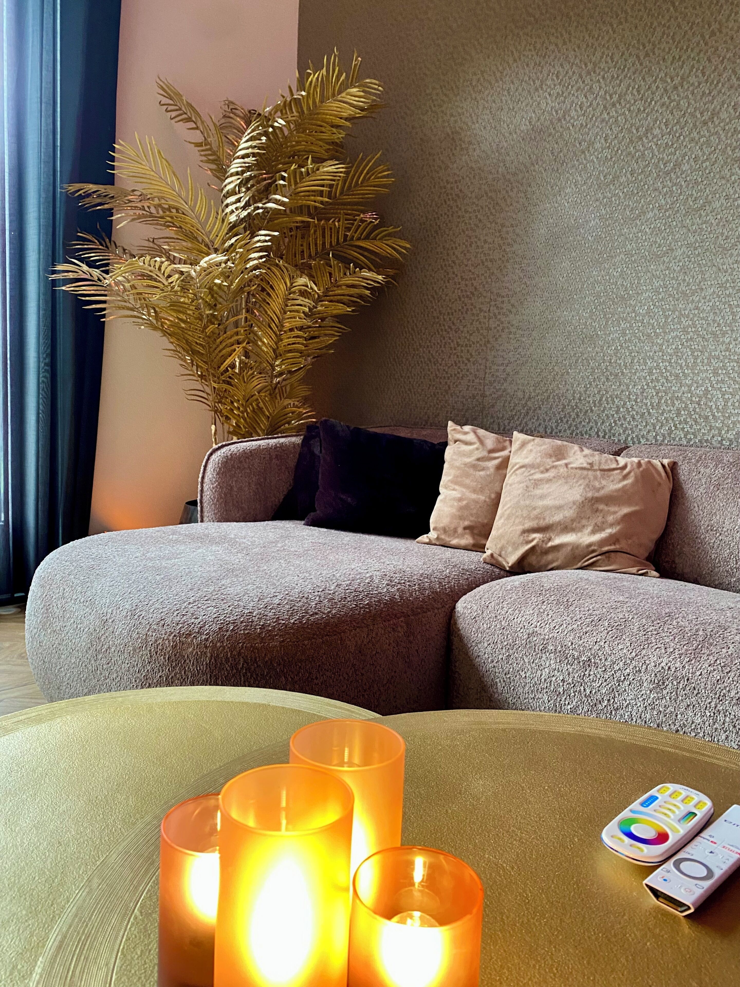 A living room with a sofa, a potted plant, and three lit candles.