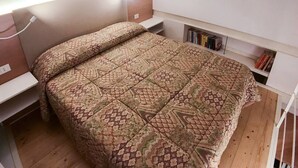 Um quarto com colcha estampada, mesas de cabeceira, mesa de apoio e uma estante com livros.