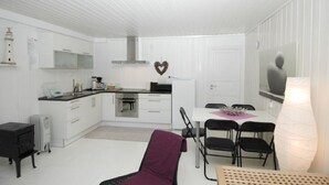 A compact, modern kitchen with white cabinetry, a central island, and a dining area with a table and chairs. - Solferie Holiday Home - Svartefjell (Kristiansand)