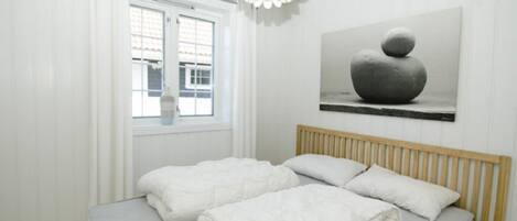 A bedroom with a bed, white curtains, a window, and a painting on the wall.