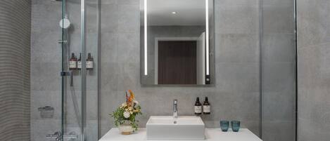 A modern bathroom with a glass-enclosed shower, a white sink, and a mirror above it.