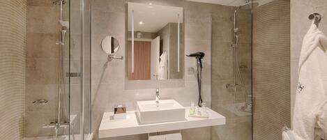 Un baño moderno con ducha de vidrio, lavamanos blanco y un espejo grande.