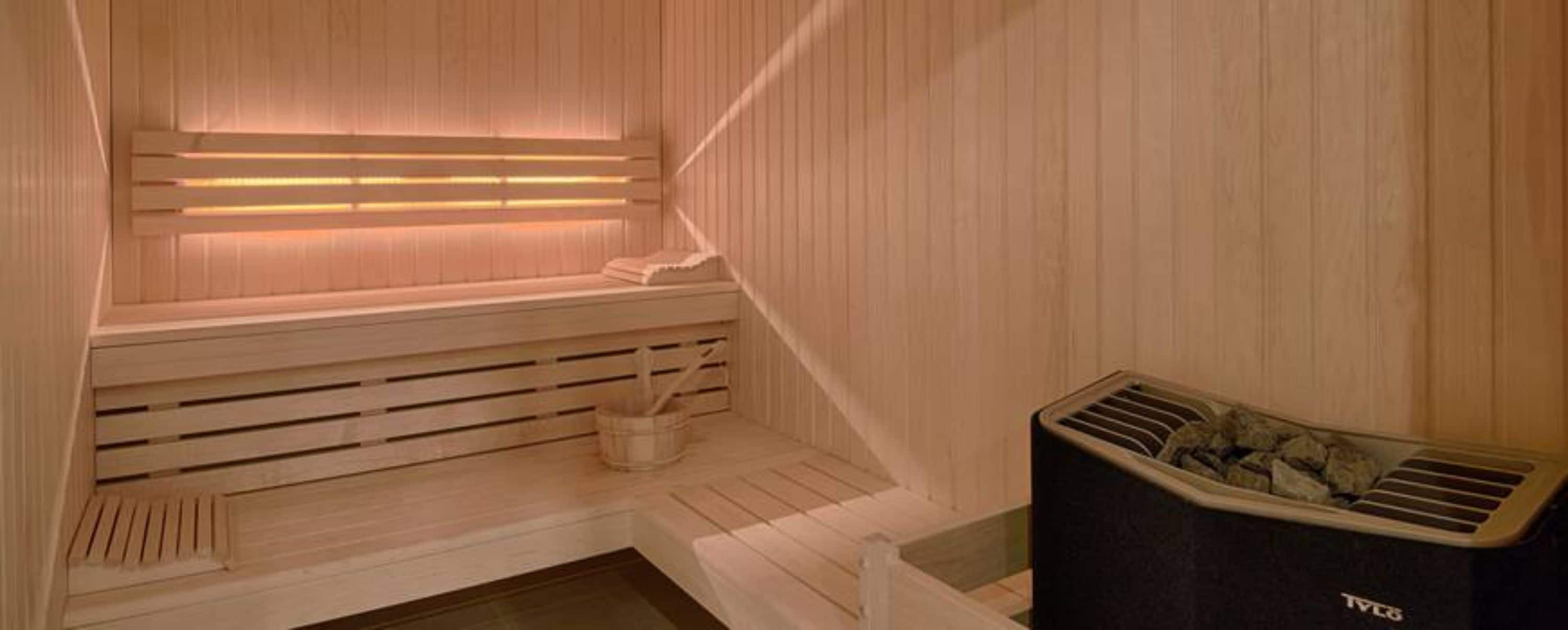 A sauna with wooden benches and a bench seat, a wooden wall, and a sauna heater.