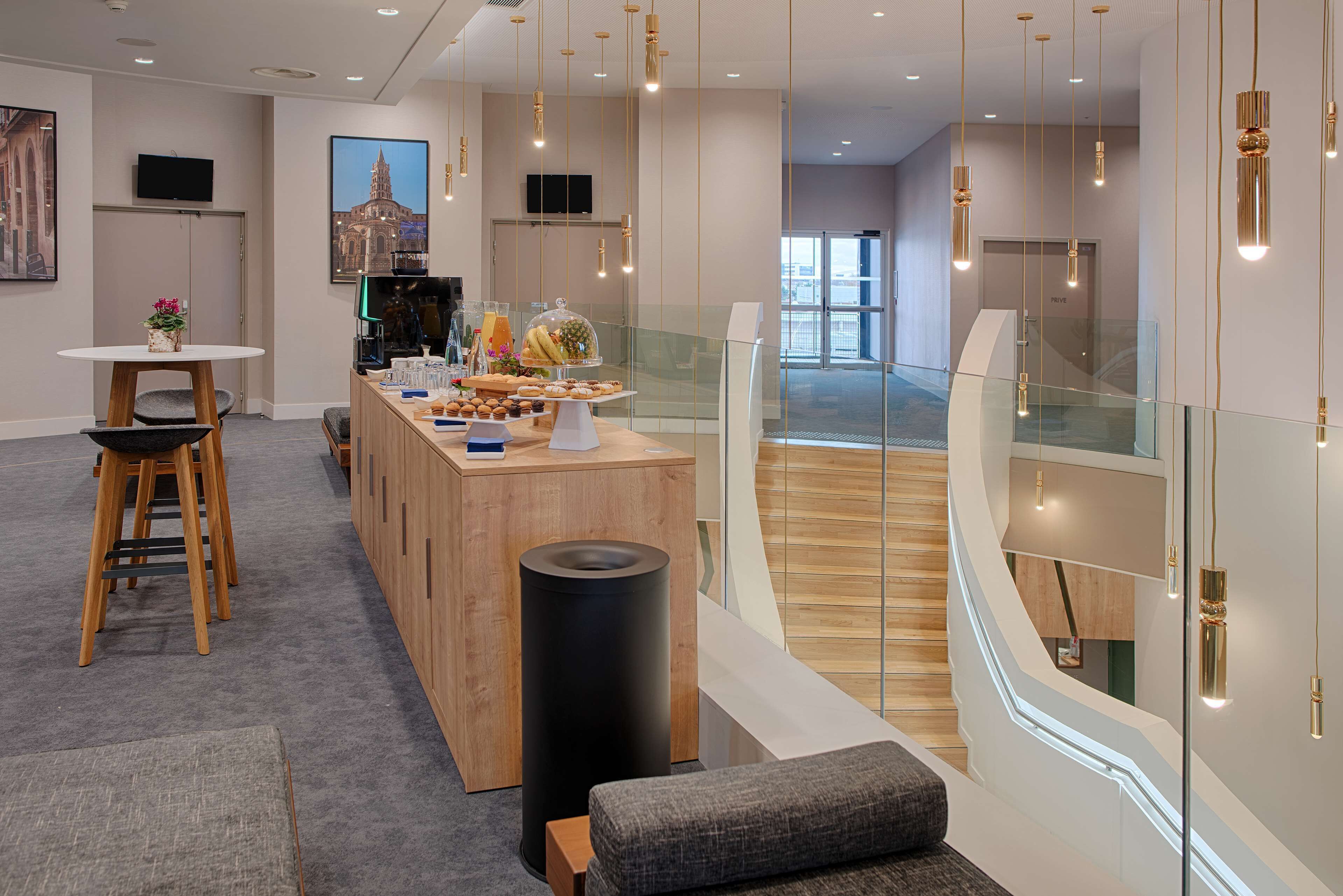 Een moderne hotel lobby met een houten receptiebalie, een koffiehoek en een glazen balustrade met uitzicht op het interieur.