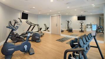 Un gimnasio moderno con máquinas de cardio, equipo de levantamiento de pesas y un espejo grande.