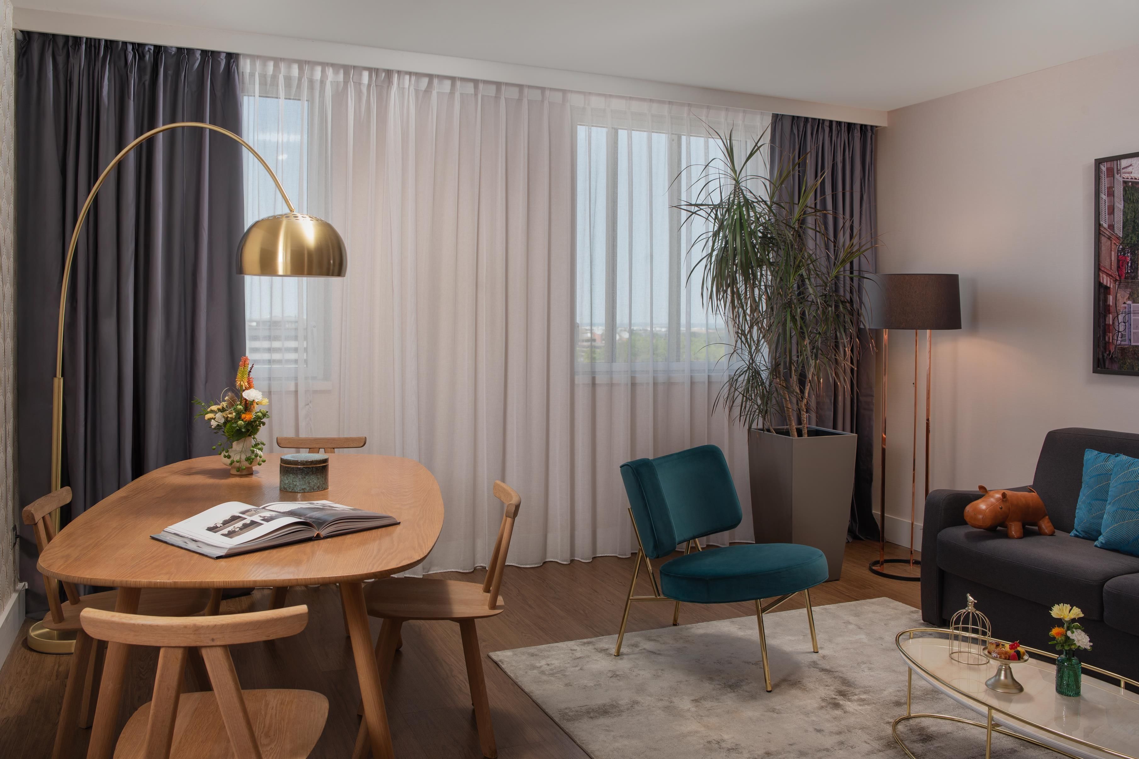 Uma sala de estar moderna com uma mesa de jantar de madeira, uma poltrona azul, um sofá e um abajur.