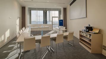 Une salle de conférence dotée d’une longue table, de chaises, d’un écran de projection et offrant une vue sur la ville grâce à de grandes fenêtres.