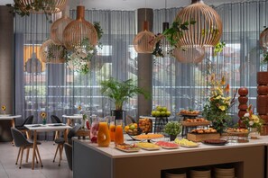 Un bufé de desayuno con diversas opciones de comida, una estación de café y plantas colgantes.