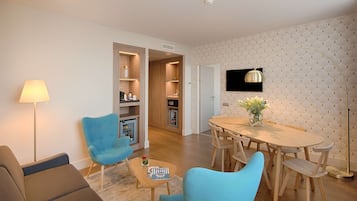 A modern living room with a sofa, two blue armchairs, a coffee table, and a dining area with a wooden table and chairs.