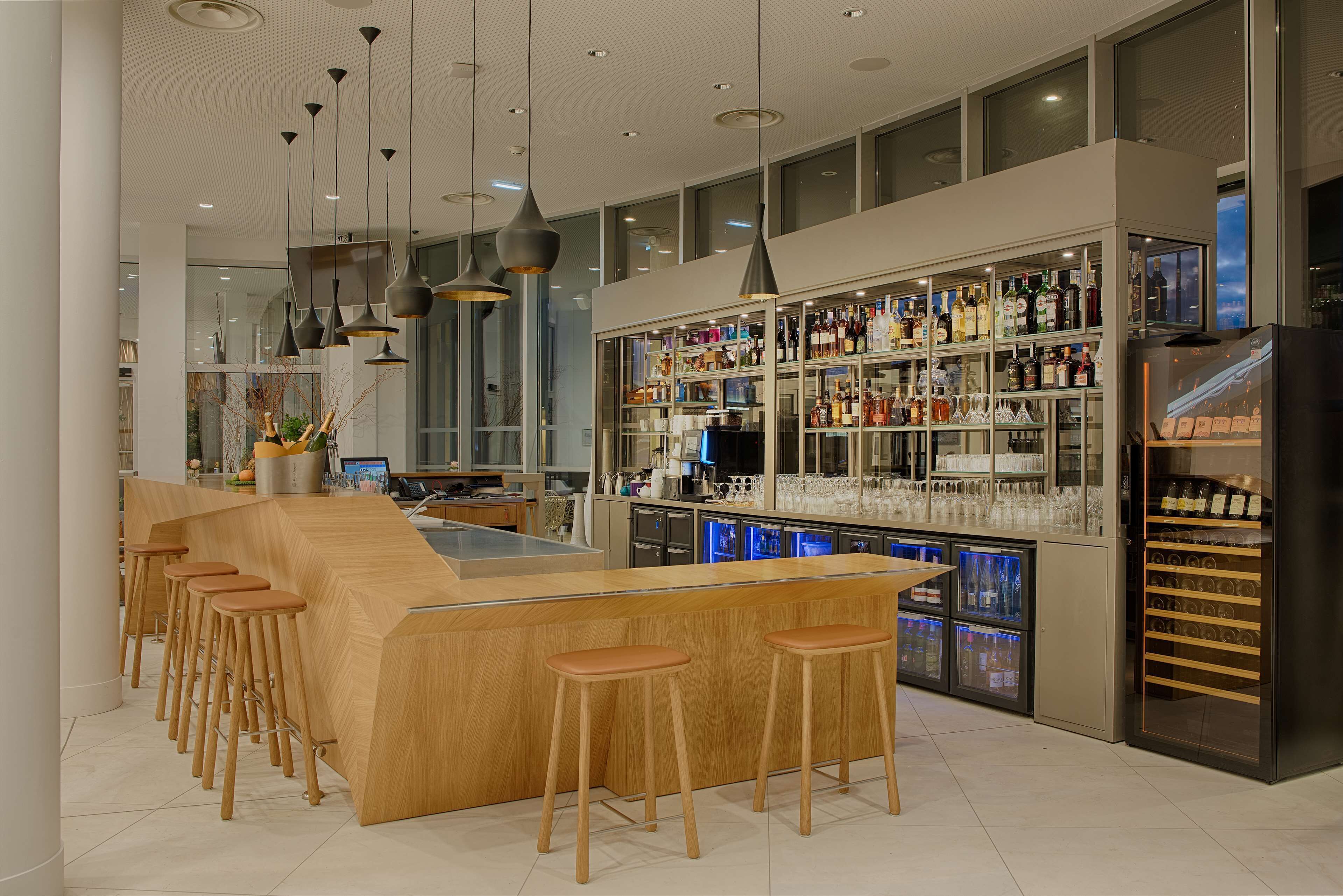 Un área de bar moderna con una barra de madera, taburetes y una estantería bien surtida de licores.