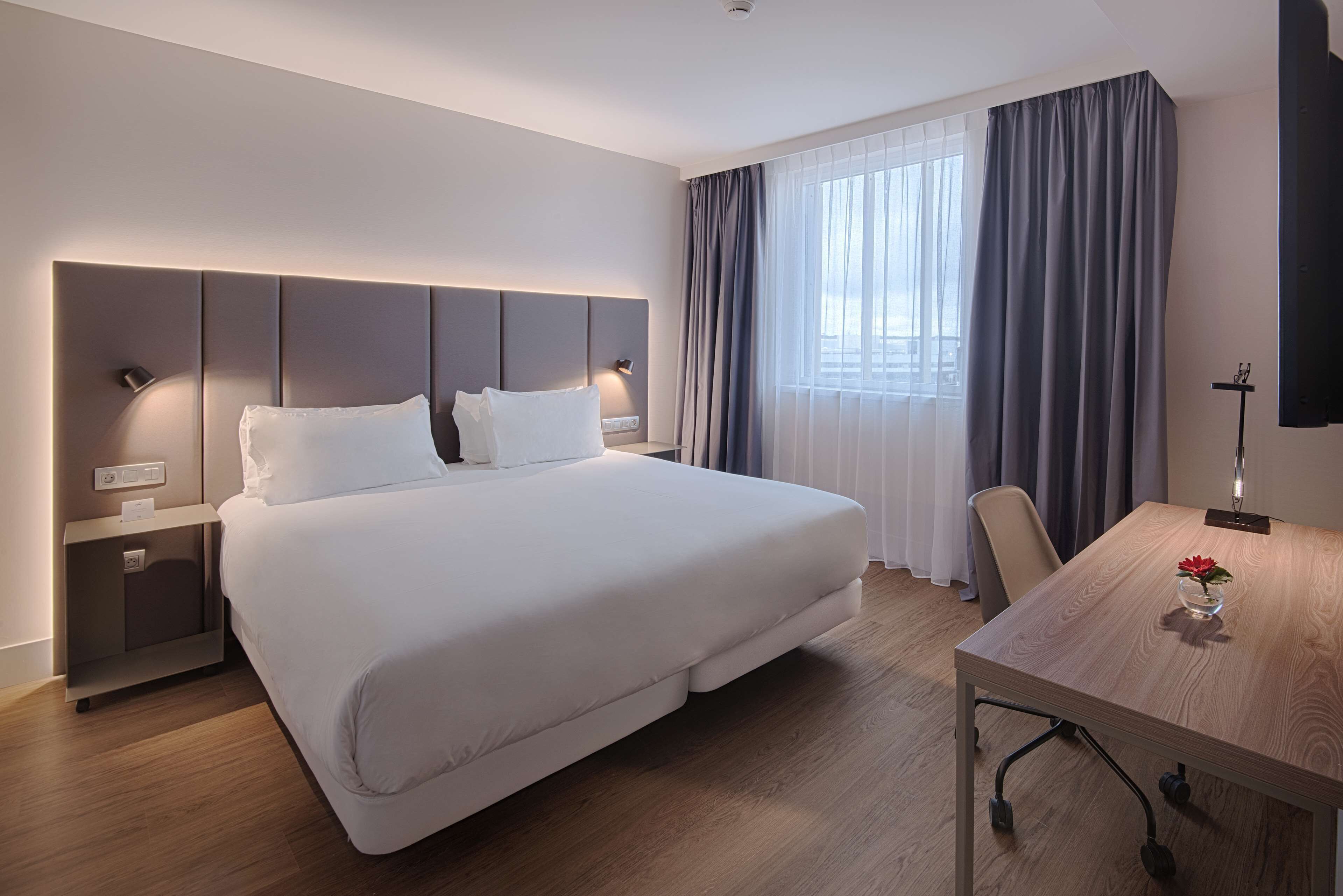 Une chambre d’hôtel moderne avec un grand lit, des tables de chevet, un bureau et une fenêtre avec des rideaux.