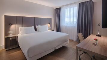 Une chambre d’hôtel moderne avec un grand lit, des tables de chevet, un bureau et une fenêtre avec des rideaux.