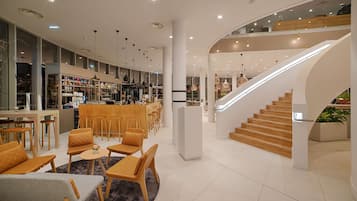 Un moderno vestíbulo de hotel con una escalera curva, zonas de estar y un bar.