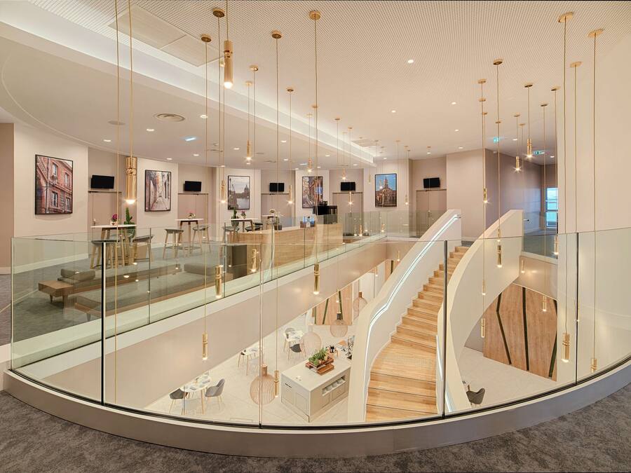 Un moderno vestíbulo de hotel con barandilla de cristal, una escalera central y obras de arte en las paredes.