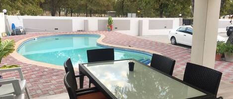 Un área de piscina con una mesa y sillas de vidrio, rodeada por un patio con baldosas.