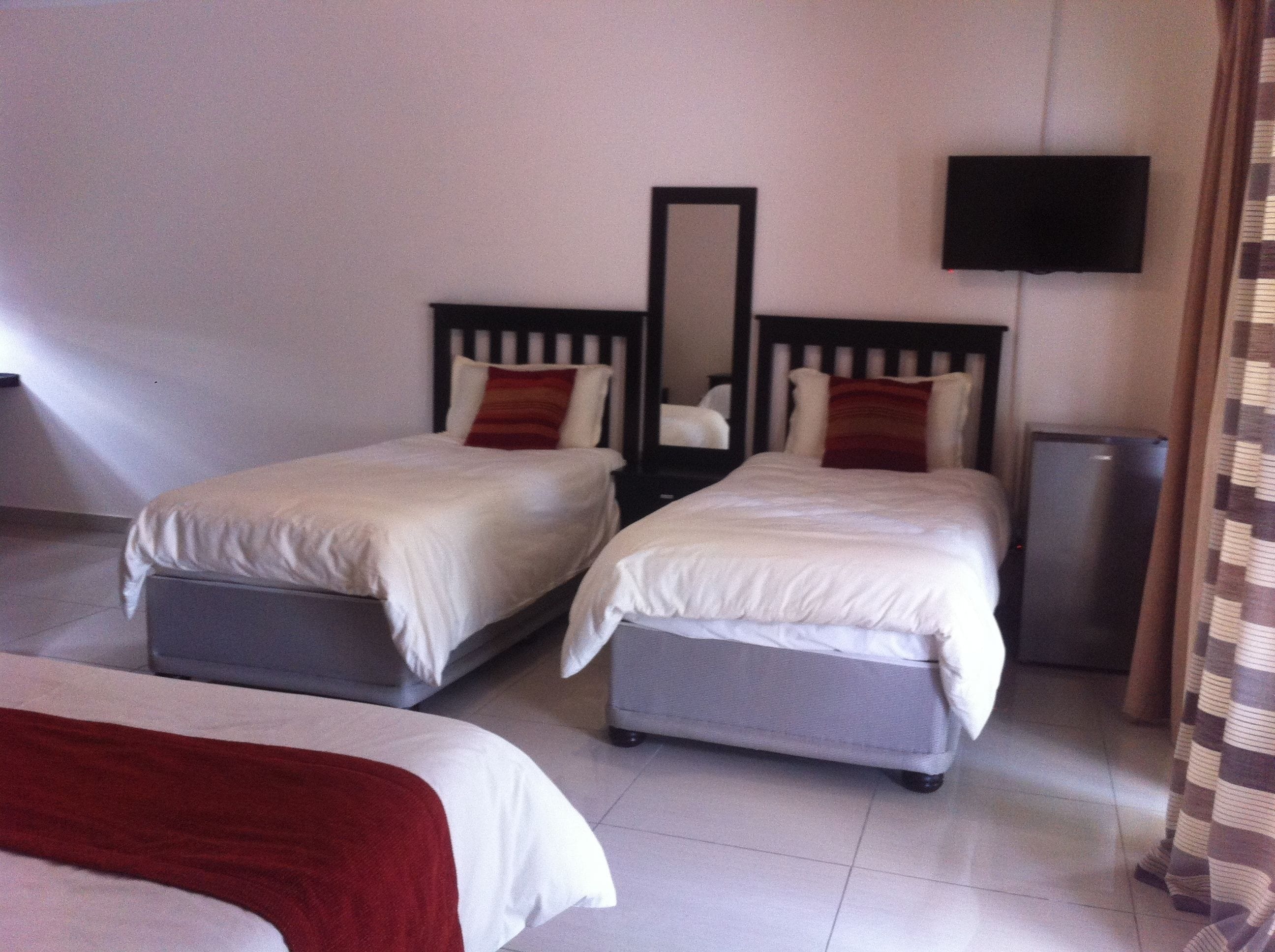 A hotel room with two single beds, a TV mounted on the wall, and a small cabinet.