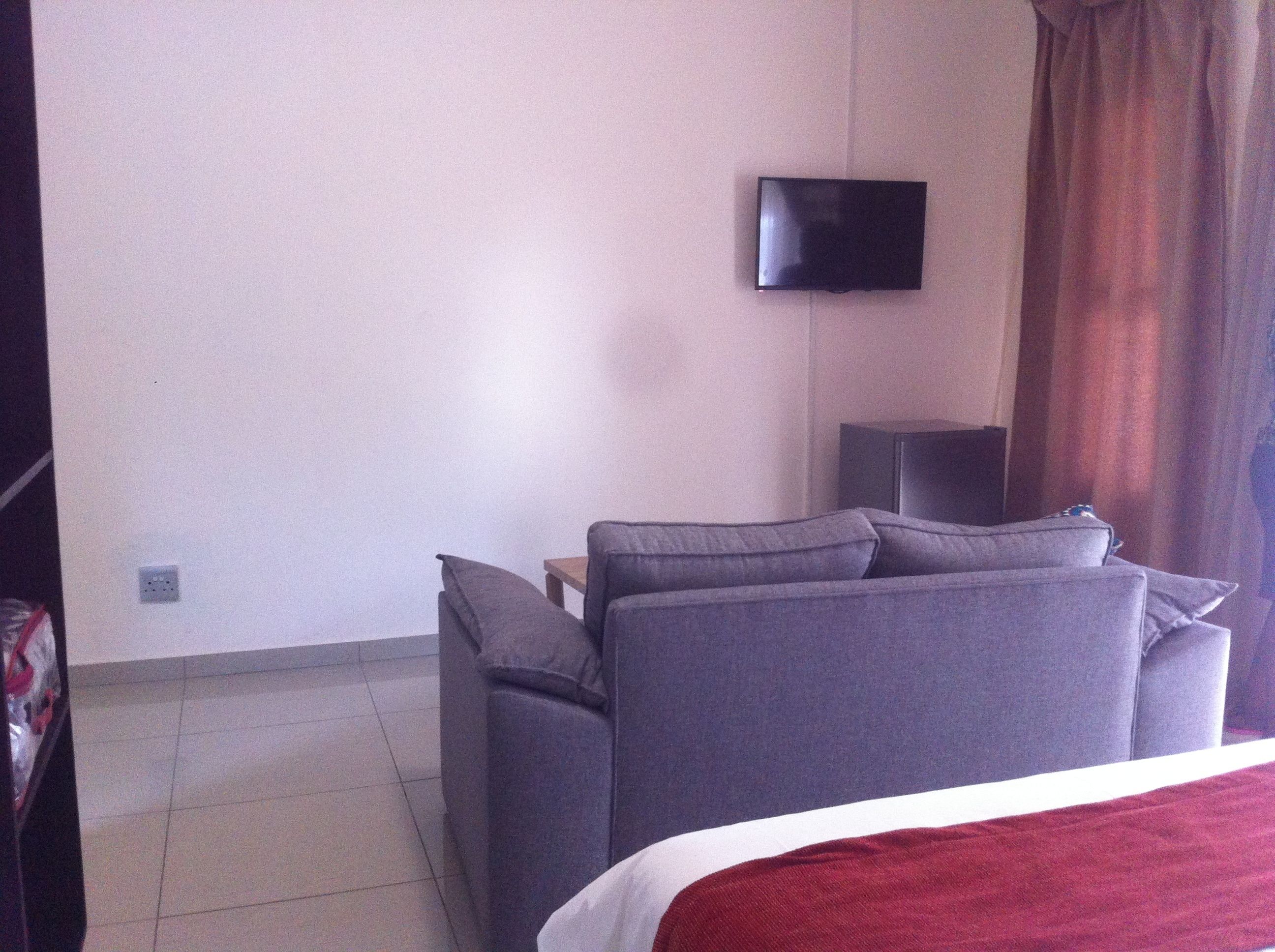 A hotel room with a bed, a grey sofa, a television mounted on the wall, and a small table.