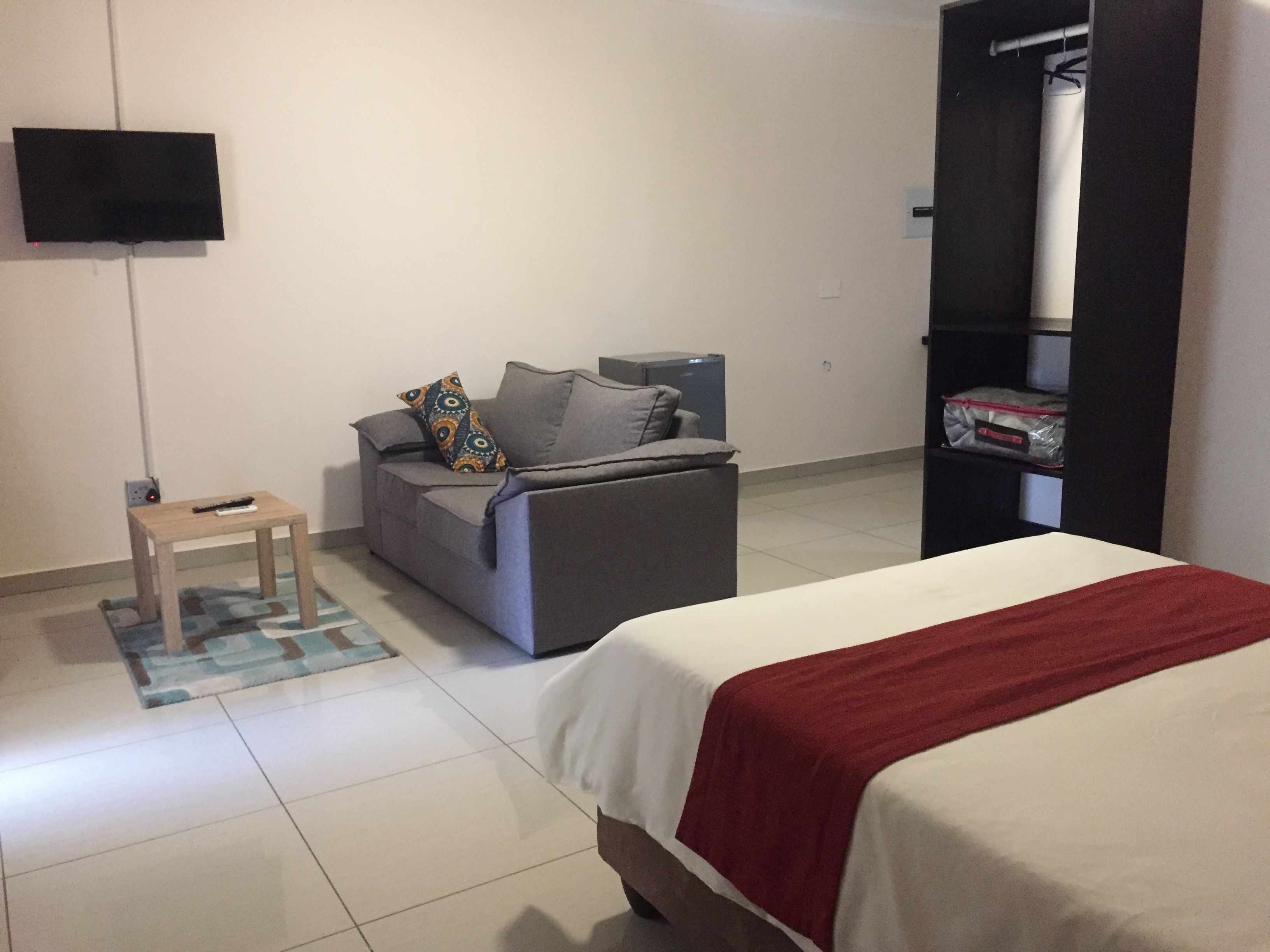 Una habitación de hotel con cama, sofá, televisión montada en la pared y armario.