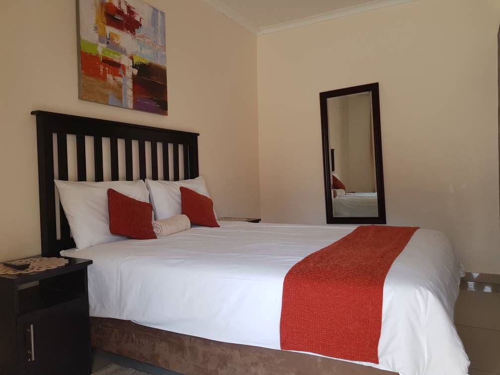 Una cama bien hecha con ropa de cama blanca y roja, un cabecero de madera, una mesita de noche con una lámpara y un espejo en la pared.