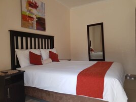 Una cama bien hecha con ropa de cama blanca y roja, un cabecero de madera, una mesita de noche con una lámpara y un espejo en la pared.