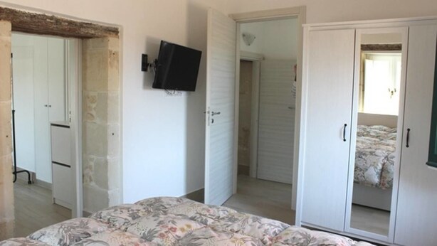 Une chambre à coucher comprenant un lit, une armoire, un téléviseur et une porte donnant sur une autre pièce.
