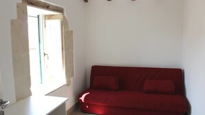 Une petite pièce avec un canapé rouge, un bureau blanc et une fenêtre donnant sur un beau paysage.