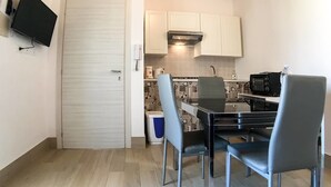 Une cuisine compacte avec un coin repas, un téléviseur fixé au mur et une porte donnant sur une autre pièce.