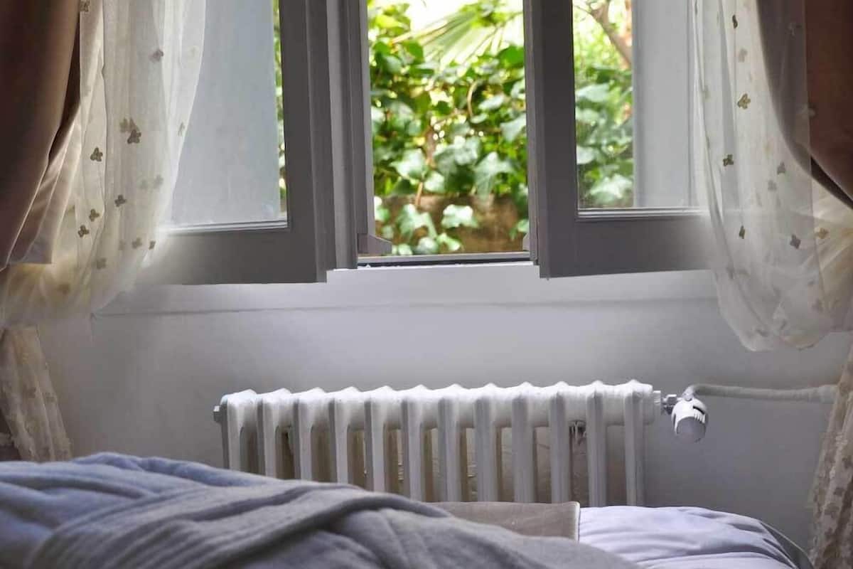 A bedroom with a bed, a window with curtains, and a radiator.