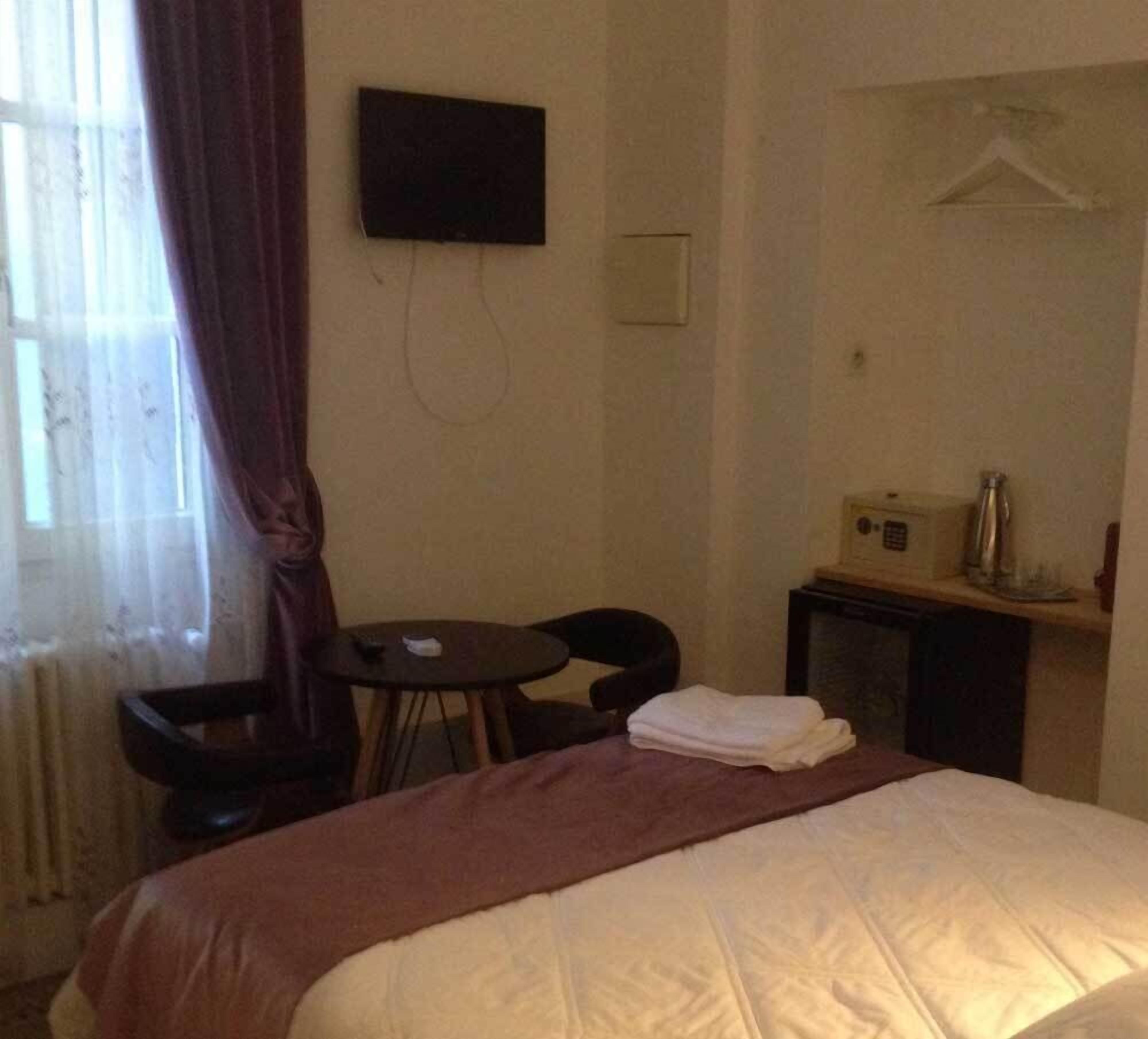 Et hotelværelse med seng, lille bord, stol, fjernsyn på væggen og et knagered.