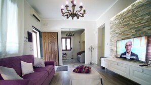 Un salón con un sofá morado, un reposapiés blanco, un televisor y una pared de piedra.