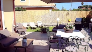 Un patio exterior con mesa y sillas, una parrilla y sillones de descanso.