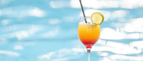 A glass of cocktail with a lime garnish by a poolside.
