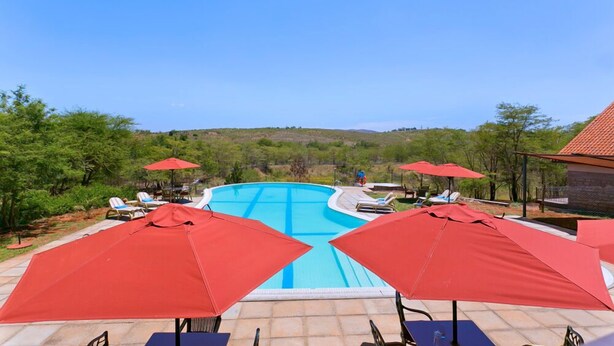 Una piscina con sombrillas rojas, sillas de descanso y vistas del paisaje circundante.
