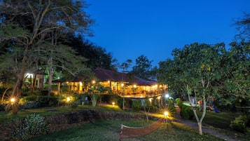 A well-lit outdoor area with a hammock, a stone wall, and a building with multiple windows and lights.