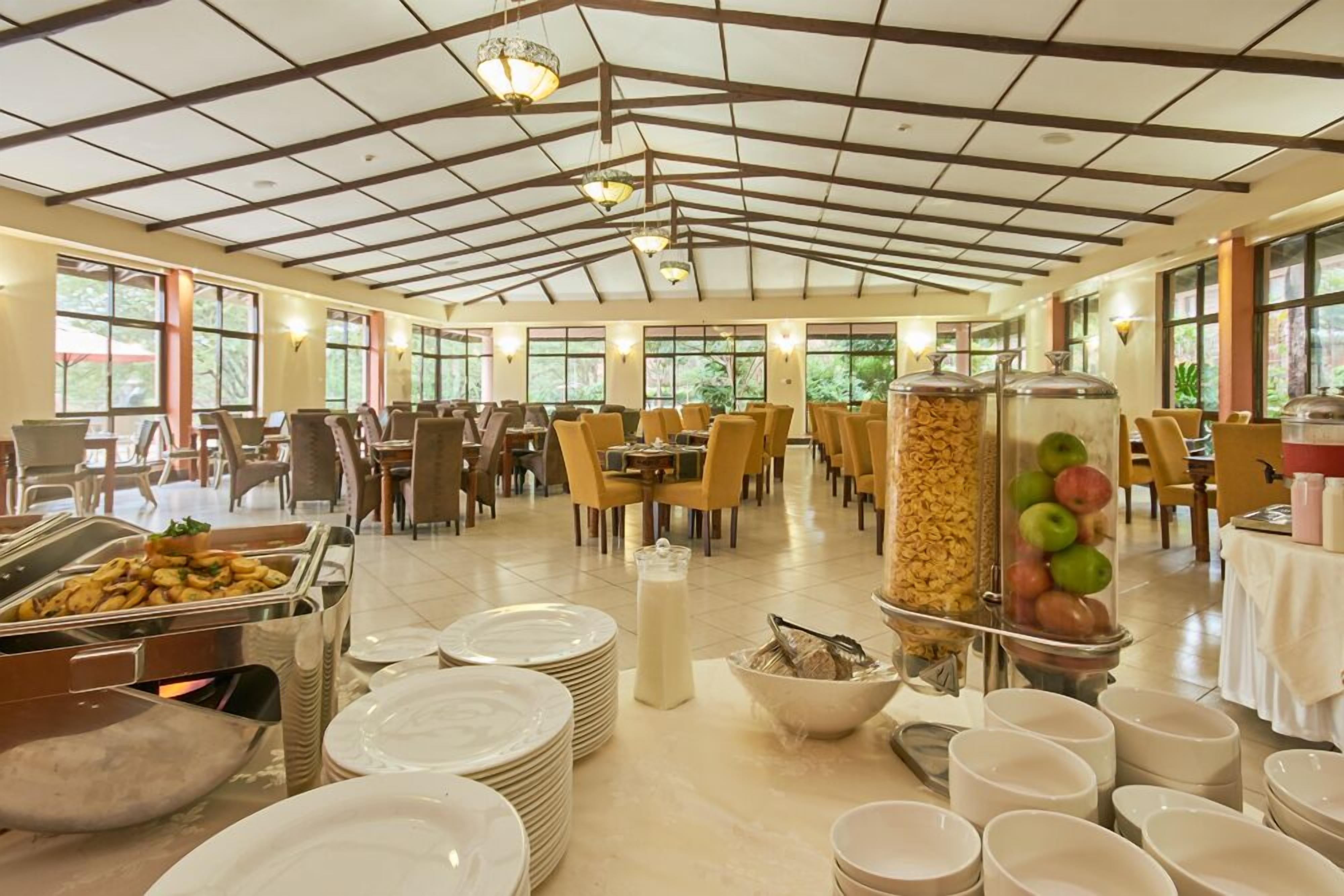 A spacious dining area with high ceilings, large windows, and a variety of food service stations including a fruit display and a buffet.