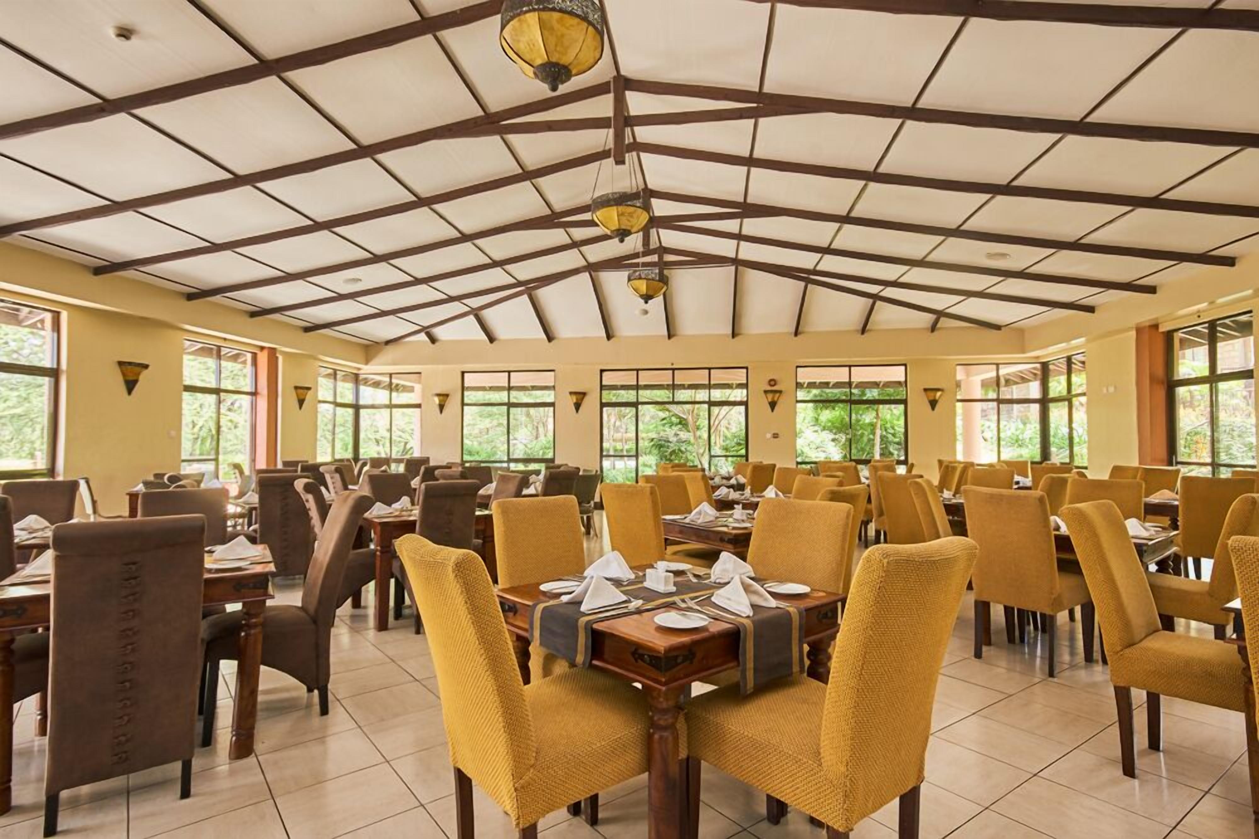 A spacious dining area with high ceilings and large windows, featuring yellow chairs and wooden tables.