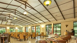 Un comedor amplio con varias mesas y sillas, ventanas grandes y un bufé con diversos alimentos.