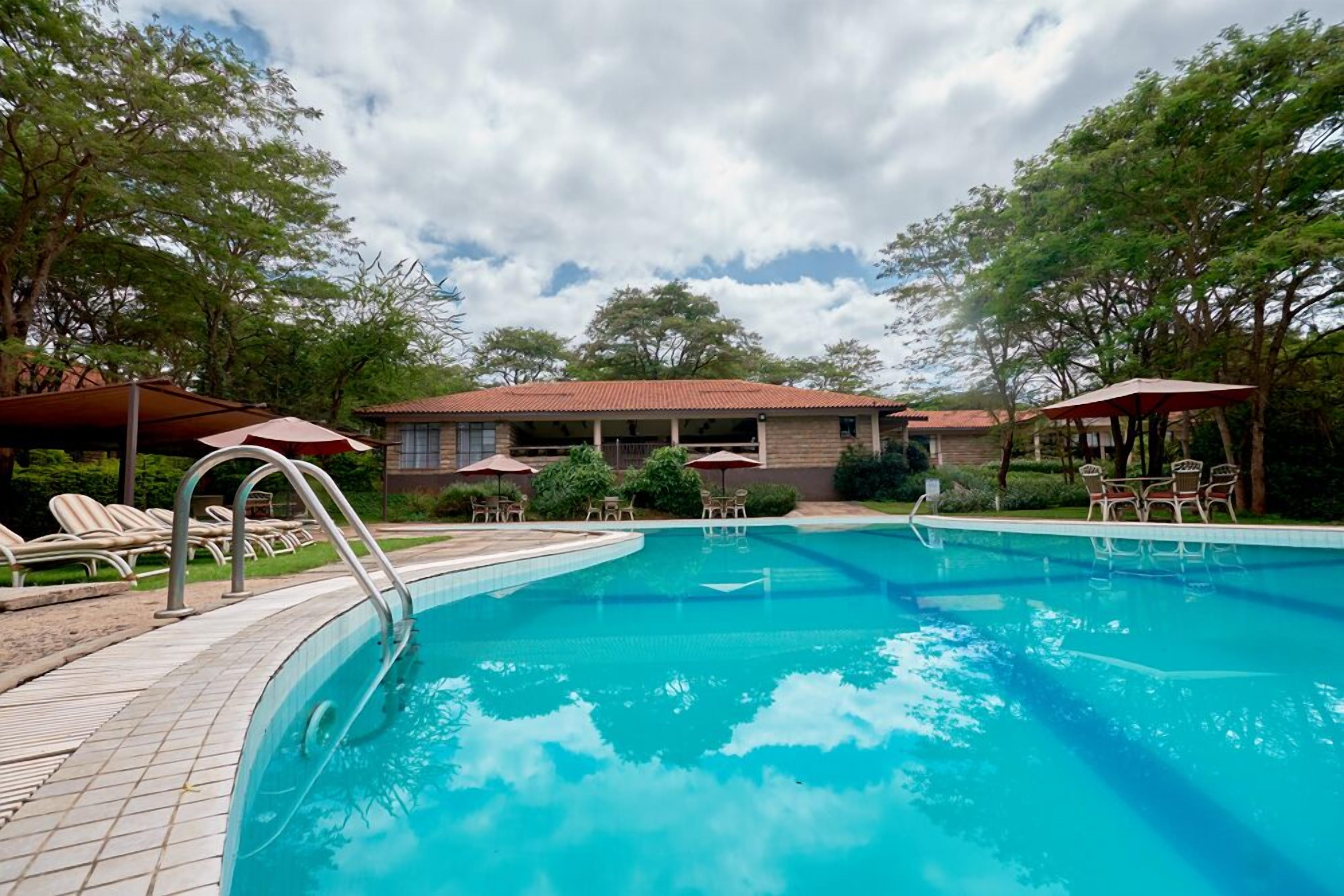 A swimming pool with lounge chairs and umbrellas, surrounded by trees and a building with a red roof.